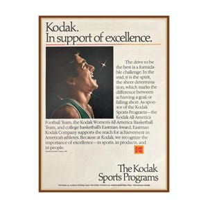 May include: Vintage Kodak advertisement in a brown frame. The ad features a black and white image of a man with his mouth open, and text that reads "Kodak. In support of excellence." The Kodak logo is visible.