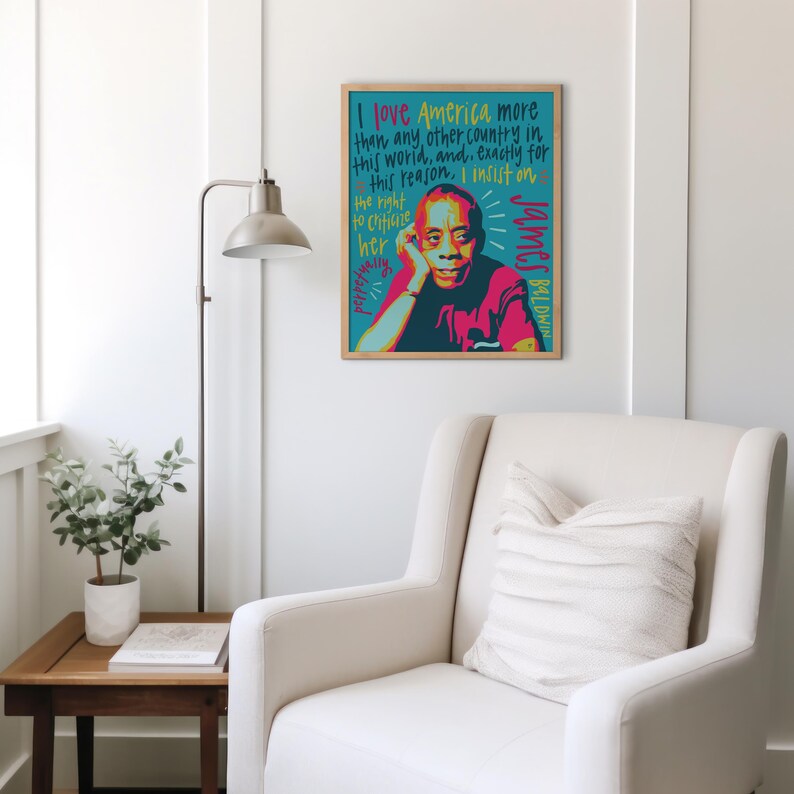 May include: A rectangular framed wall art print featuring a stylized portrait of James Baldwin in shades of pink, red, and dark blue. The background is teal with hand-lettered text in yellow and dark blue that reads, I love America more than any other country in this world, and, exactly for this reason, I insist on the right to criticize her perpetually.