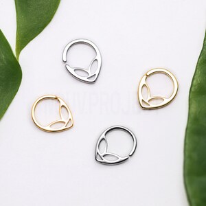 May include: Four silver and gold nose rings with a unique alien-like design. The rings are all open hoop style and have a teardrop shape with a cut-out design.