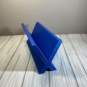 May include: A vibrant blue book stand with an X-shaped base. The stand has a sleek, modern design, perfect for displaying books or magazines. The stand is made of a solid material and is placed on a wooden surface.
