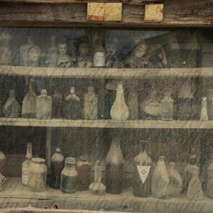 Puede incluir: Un armario de madera con puertas de cristal exhibe una colección de botellas y tarros de vidrio antiguos en múltiples estantes. Las botellas varían en forma y tamaño, algunas con tapones. El armario tiene un aspecto rústico y envejecido.