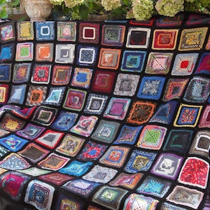 May include: A colorful crocheted blanket made of squares in various colors and patterns. The blanket is made with black yarn and features a variety of colors, including red, blue, green, and purple.