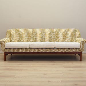 Könnte beinhalten: Ein Vintage-Sofa aus der Mitte des Jahrhunderts. Es hat einen gemusterten gelb-weißen Stoff, drei weiße Kissen und einen dunklen Holzrahmen mit vier Beinen. Das Sofa ist ein stilvolles Möbelstück, ideal für ein Wohnzimmer.
