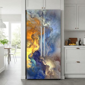 a refrigerator with a vibrant, abstract painting covering its surface. The painting is a mix of blue, orange, and yellow colors, creating a dynamic and eye-catching design. The refrigerator is located in a kitchen, with a dining table and chairs visible in the background.