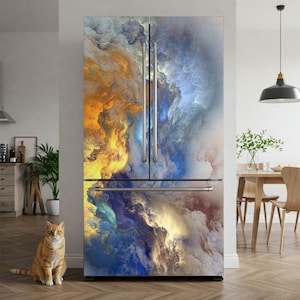 a large refrigerator with a vibrant, abstract painting covering its surface. A cat is sitting on the floor in front of the refrigerator, and there is a dining table and chairs visible in the background.