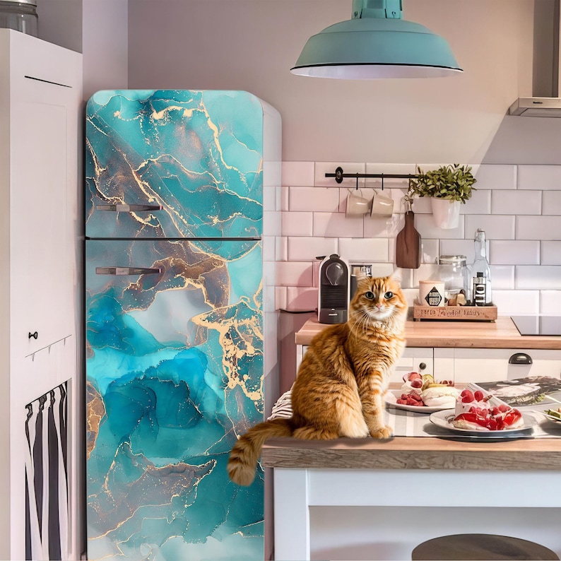 A cat sits on a kitchen counter, with a turquoise and gold marble-patterned refrigerator in the background.