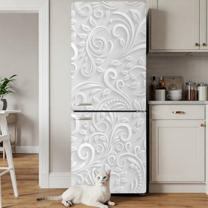 May include: A white refrigerator with a decorative floral design. The design features swirling patterns of leaves and vines in a raised relief. A white cat with blue eyes is lying on the floor in front of the refrigerator.