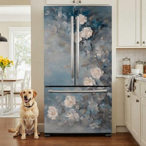 May include: A refrigerator with a floral design. The front of the fridge is covered in a blue and gray mural with white flowers and green leaves. The fridge has stainless steel handles and is in a kitchen with a dog.