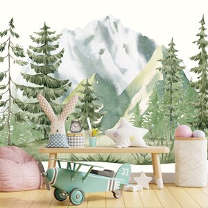 Puede incluir: Una ilustración de acuarela de una cordillera con árboles verdes y un pico nevado. La ilustración está impresa en una pared, con un avión de juguete, una silla de puf y un banco de madera delante.