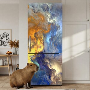 A large, colorful abstract painting is displayed on the side of a refrigerator, with a small brown capybara sitting next to it.