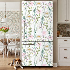 May include: A white refrigerator with a floral design featuring daisies, pink flowers, and green leaves. The pattern covers the entire front of the appliance, creating a decorative kitchen element. A dog is lying on the floor in front of the refrigerator.