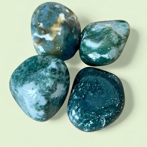 May include: Four polished moss agate stones with smooth, rounded surfaces. The stones feature deep forest green, translucent white, and earthy brown inclusions, creating unique patterns of moss-like formations within each individual gemstone.