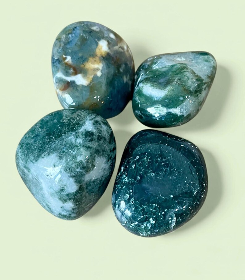 May include: Four polished moss agate stones with smooth, rounded surfaces. The stones feature deep forest green, translucent white, and earthy brown inclusions, creating unique patterns of moss-like formations within each individual gemstone.