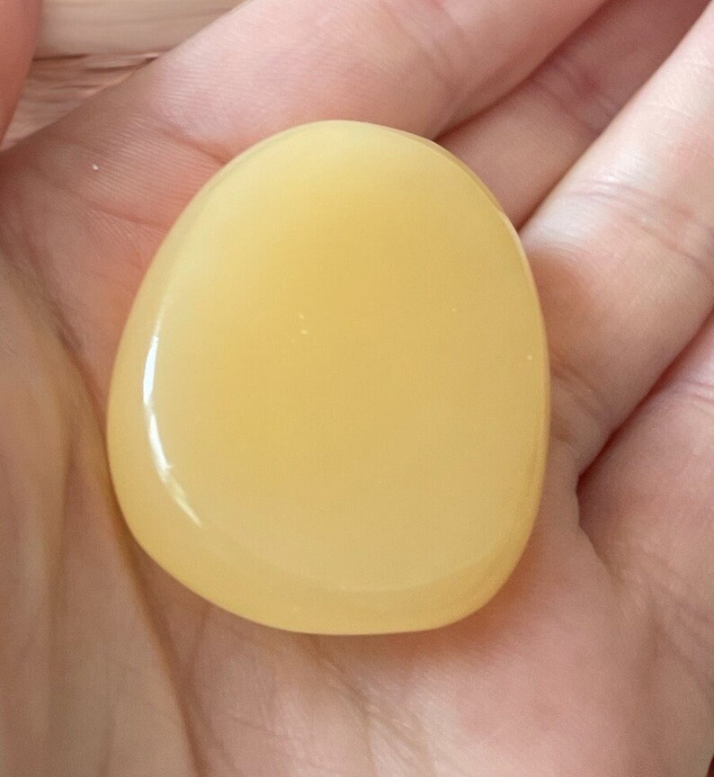 May include: A smooth, pale yellow, oval-shaped polished stone.