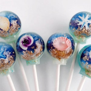May include: A collection of six colorful lollipops with a blue and white swirl design. Each lollipop features a different seashell design, including a starfish, a clam, and a scallop.