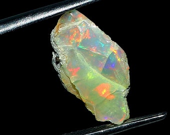 May include: A rough, irregular shaped opal gemstone with a milky white base and flashes of iridescent green, orange, and red.