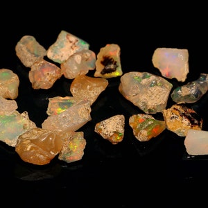 Puede incluir: Una colección de piedras preciosas de ópalo en bruto de varios tamaños y formas. Los ópalos son una mezcla de colores blancos, transparentes e iridiscentes.