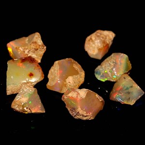 May include: A group of seven rough, natural opal stones. The opals are a mix of white, yellow, and orange with iridescent flashes of color.