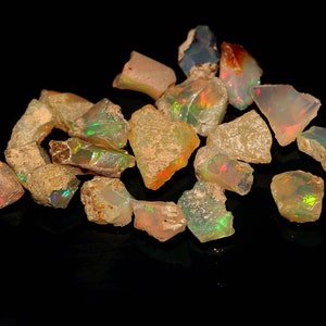 Könnte beinhalten: Eine Sammlung von rohen, natürlichen Opal-Edelsteinen in verschiedenen Schattierungen von Weiß, Braun und Grün mit irisierenden Farbschimmern. Die Opale sind unregelmäßig geformt und haben eine raue, unpolierte Oberfläche.
