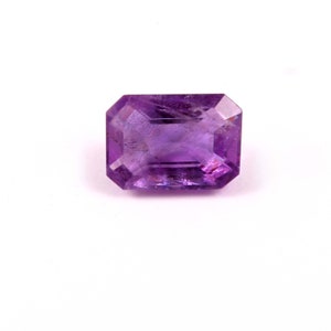 Puede incluir: Una piedra preciosa de amatista de color púrpura intenso tallada en forma de esmeralda.