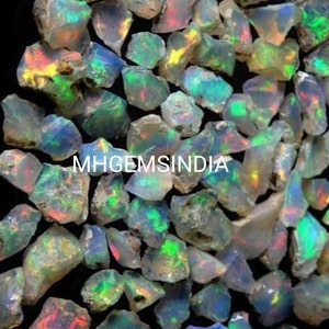 Puede incluir: Una colección de piedras preciosas de ópalo natural en bruto. Los ópalos son una mezcla de colores blancos, grises e iridiscentes, con destellos de verde, azul y rojo. Los ópalos son de forma y tamaño irregulares, y algunos tienen una superficie rugosa y texturizada.