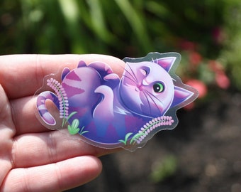 May include: A purple and pink cat sticker with a white face and green eyes. The cat is lying on its back with its paws in the air. The sticker is surrounded by pink flowers.