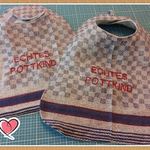 Könnte beinhalten: Zwei weiße und blaue karierte Lätzchen mit rotem Sticktext "Echtes Pottkind".