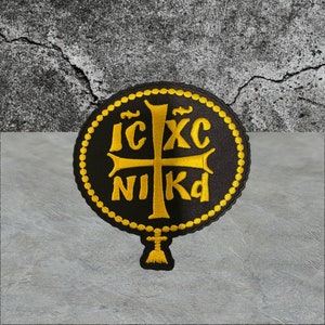 May include: A black embroidered patch with a gold cross and the text "IC XC NIKA" in a circle.