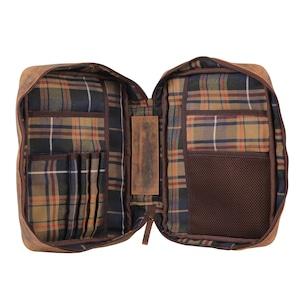 May include: An open brown leather organizer case featuring a plaid fabric interior lining. The left side includes multiple vertical slots for pens or tools, while the right side contains a mesh pocket. A central leather strap connects both sides.