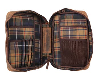 May include: An open brown leather organiser case featuring a plaid fabric interior lining. The left side includes multiple vertical slots for pens or tools, while the right side contains a mesh pocket. A central leather strap connects both sides.
