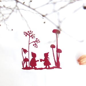 May include: A red paper cut-out of two children holding hands, surrounded by stylized plants and flowers. The image is set against a white background with dried branches and a bottle stopper.