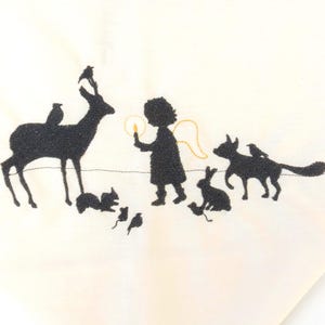May include: Cream-colored fabric with a black silhouette design featuring a deer, birds, squirrels, a child with wings, foxes, and rabbits. The child holds a glowing object, and the animals surround them.