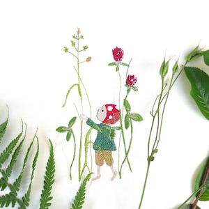 May include: Embroidered design of a small person wearing a red mushroom hat, holding a green plant. The design is surrounded by green fern leaves and a branch with green leaves.