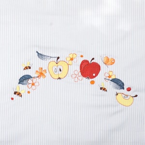 May include: White fabric with a blue and white striped pattern. The fabric is embroidered with a design of red and yellow apples, bees, butterflies, and flowers.