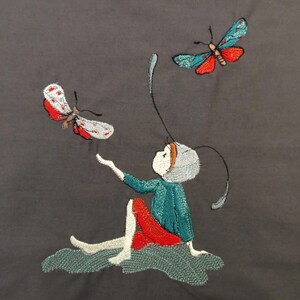 Può includere: Immagine ricamata di una figura seduta con il braccio teso, che interagisce con due farfalle. La figura indossa un top turchese e una gonna rossa. Le farfalle hanno ali rosse, bianche e turchesi. Lo sfondo è grigio.