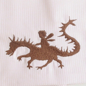 May include: A pink linen napkin with a brown embroidered design of a person riding a dragon.