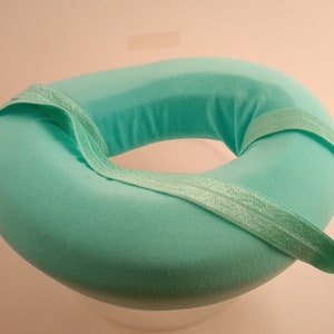 May include: A light green donut-shaped cushion with a light green elastic band around the outside.