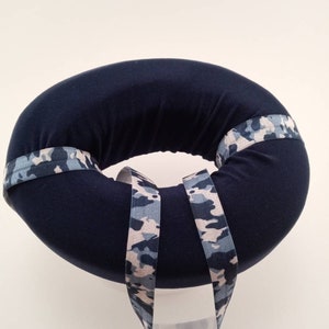 May include: A dark blue donut-shaped cushion with a camouflage pattern fabric trim. The cushion is designed to provide support and comfort.