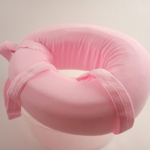 May include: A pink donut-shaped pillow with a white elastic band around the center.