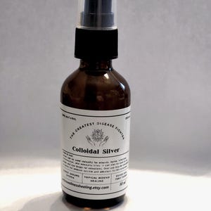 Könnte beinhalten: Eine braune Glasflasche mit schwarzem Sprühkopf und weißem Etikett. Das Etikett trägt die Aufschrift "Colloidal Silver" und "The Greatest Disease Fighter". Die Flasche enthält 60 ml Flüssigkeit und ist als 100% natürlich gekennzeichnet.