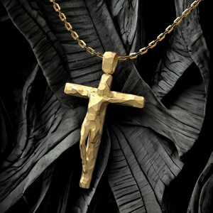 May include: A gold-colored pendant necklace featuring a textured cross design. The cross is suspended from a matching gold chain. The background is a dark, textured surface.