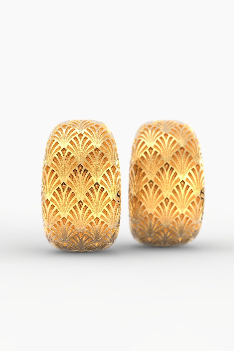 Puede incluir: Dos pendientes dorados de estilo Art D&eacute;co. Cada pendiente tiene forma ovalada con un patr&oacute;n detallado en forma de abanico. Los pendientes est&aacute;n sobre un fondo blanco, resaltando su intrincado dise&ntilde;o y brillo met&aacute;lico.