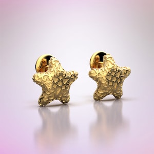 May include: A pair of gold star-shaped earrings with intricate detailing. The earrings are on a white background.