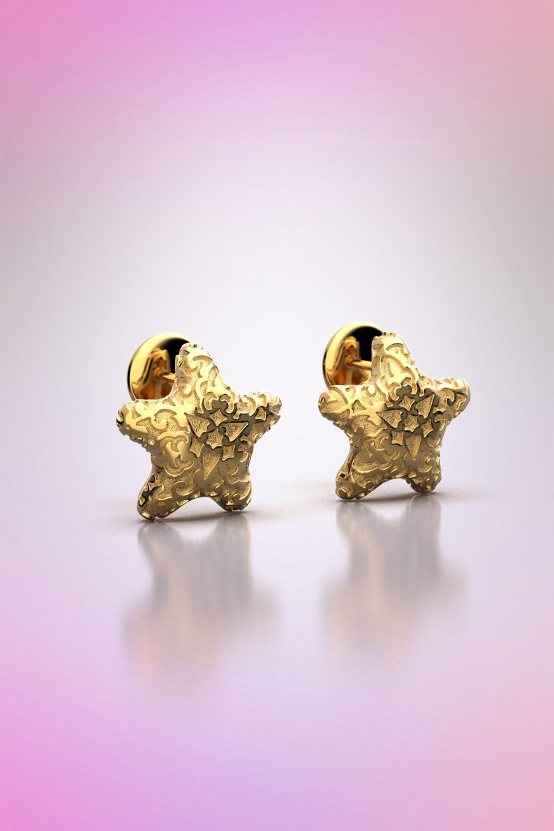 May include: A pair of gold star-shaped earrings with intricate detailing. The earrings are on a white background.