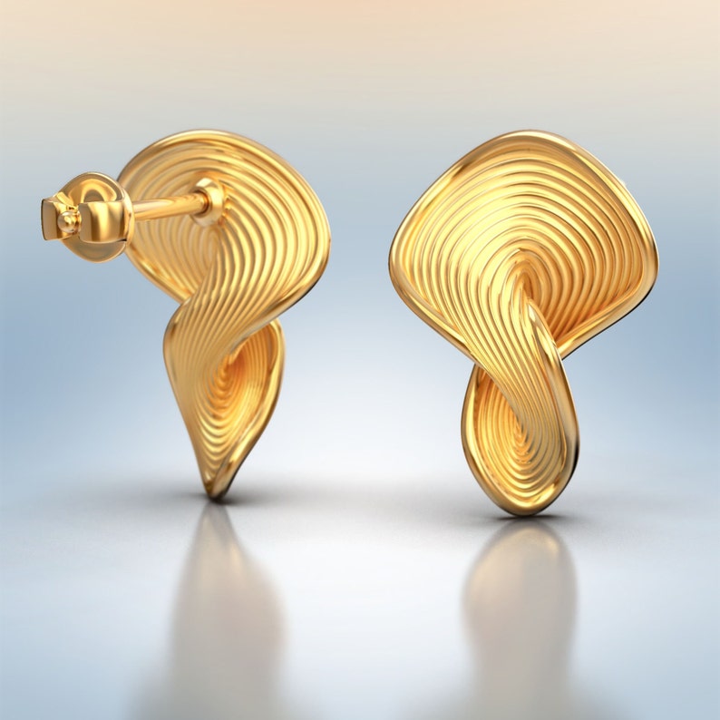 May include: A pair of gold-toned earrings with a twisted, wave-like design. The earrings have a smooth, polished finish.