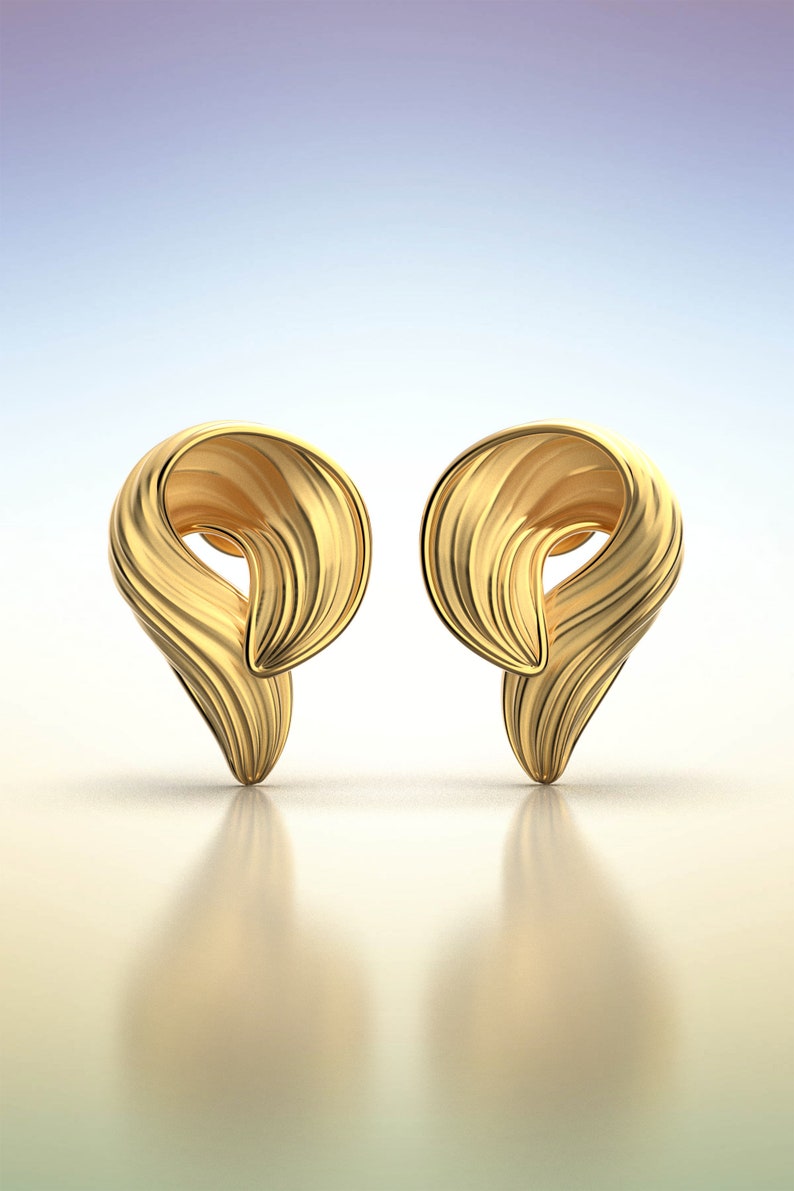 Puede incluir: Un par de pendientes de color dorado con un dise&ntilde;o &uacute;nico y abstracto. Los pendientes tienen forma de una ola retorcida y fluida.