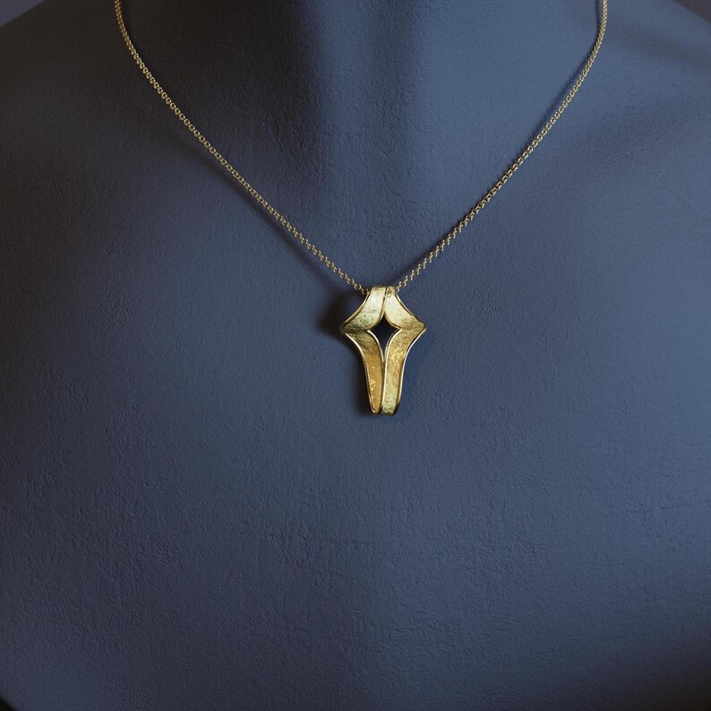 May include: A gold-colored pendant necklace with a unique, abstract design. The pendant has a textured surface and a central, dark-colored void. The necklace chain is delicate and also gold-toned, creating a cohesive jewelry piece.