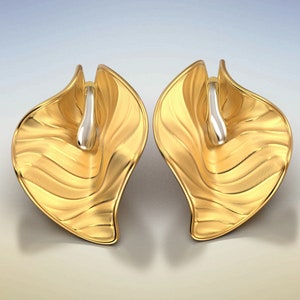 Puede incluir: Un par de pendientes de oro con un dise&ntilde;o ondulado en forma de hoja. Los pendientes tienen un acento plateado en el centro.