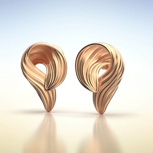 Puede incluir: Un par de pendientes de color dorado con un dise&ntilde;o &uacute;nico y abstracto. Los pendientes est&aacute;n hechos de un metal liso y brillante y tienen una forma retorcida y ondulada.