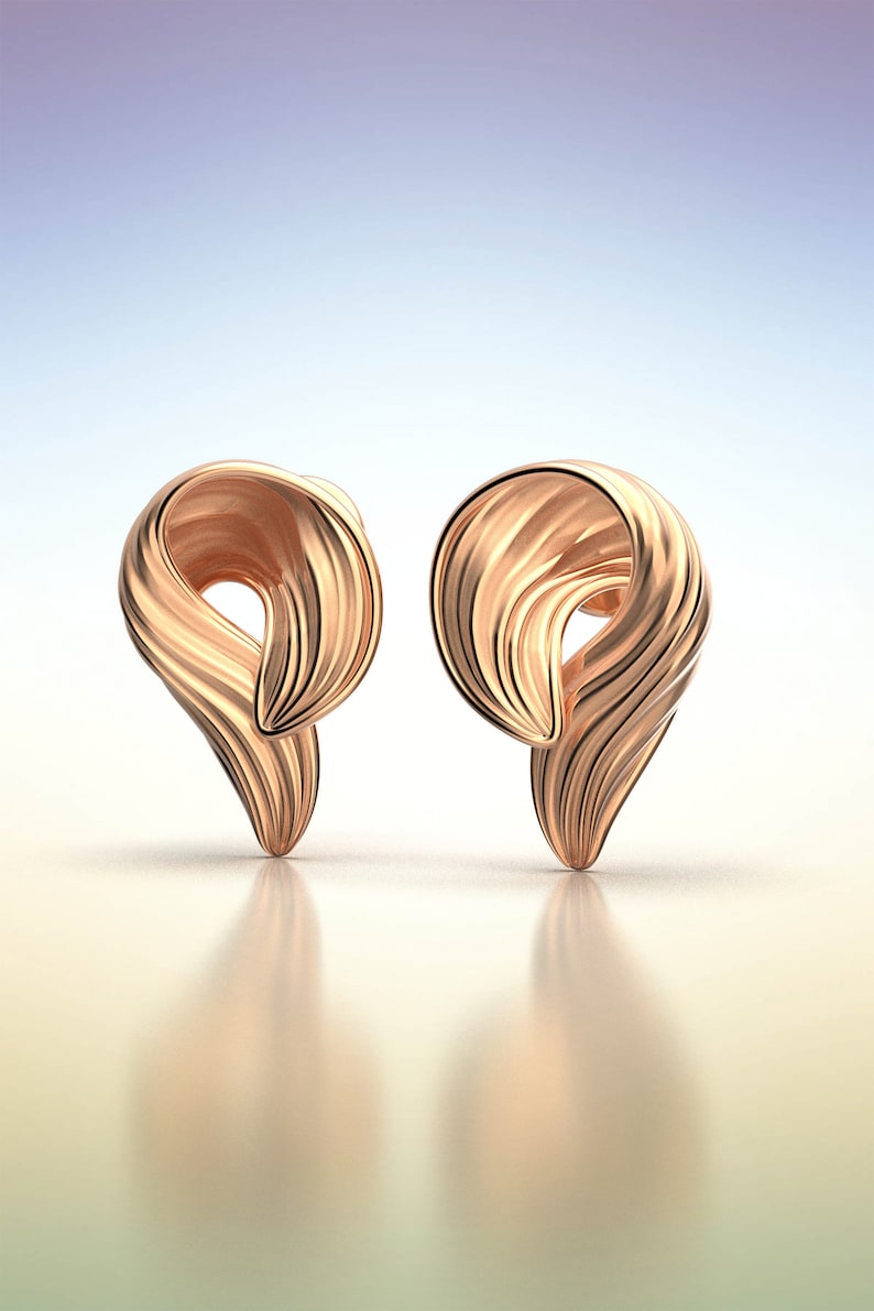Puede incluir: Un par de pendientes de color dorado con un dise&ntilde;o &uacute;nico y abstracto. Los pendientes est&aacute;n hechos de un metal liso y brillante y tienen una forma retorcida y ondulada.